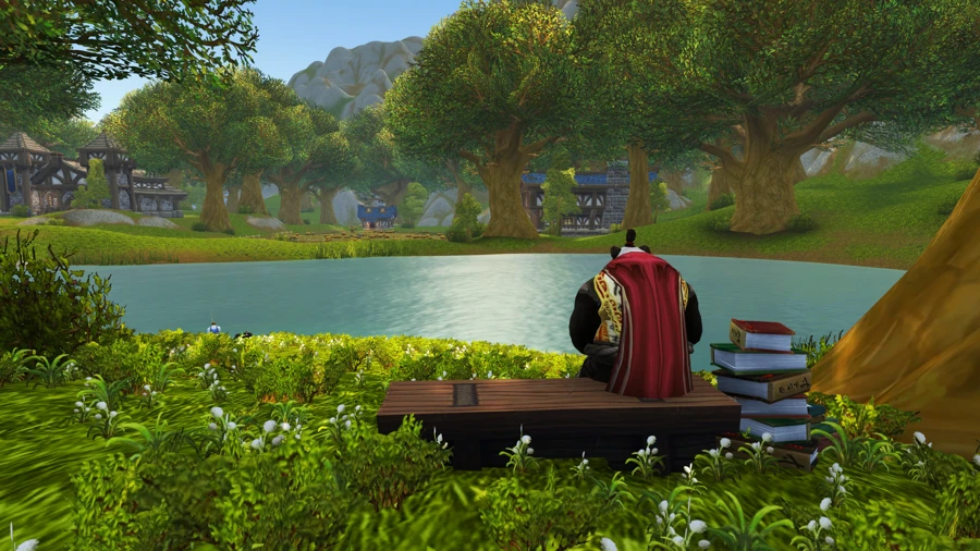 a pandaren sitting on a bench facing away toward a pond with a stack of books next to him